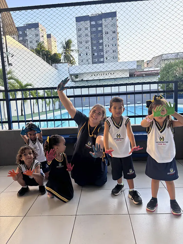 Crianças da Educação Infantil com as mãos pintadas ao lado da professora